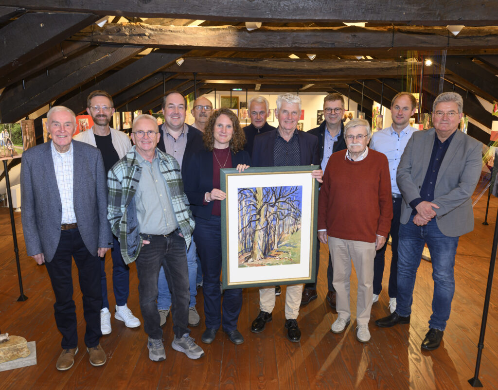 Gruppe von Personen, die ein Kunstwerk in einem Ausstellungsraum präsentieren, umgeben von weiteren Kunstwerken.