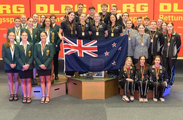 Gruppenfoto von Sportlern mit Medaillen und der neuseeländischen Flagge bei einer Veranstaltung.