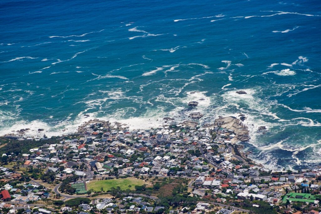 Luftaufnahme einer Küstenstadt mit Wellen, die gegen die Felsen schlagen, und Häusern in der Nähe des Wassers.