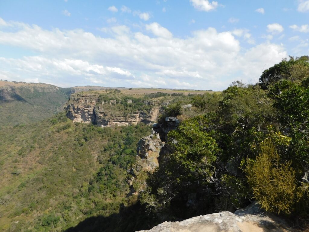 Blick auf eine grüne Landschaft mit Klippen und bewaldeten Hängen in der Ferne.