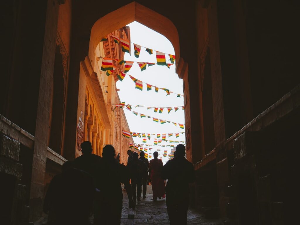 Menschen gehen durch einen Torbogen, umgeben von bunten Fahnen in einem historischen Gebäude.