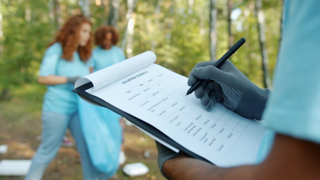 Person mit Handschuhen hält ein Notizbuch mit einer Tabelle zur Erfassung von Freiwilligenaktivitäten im Freien.