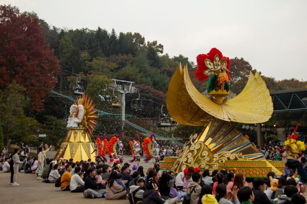 Bunte Festwagen mit aufwendigen Designs während einer Parade in einem Park mit Zuschauern im Vordergrund.