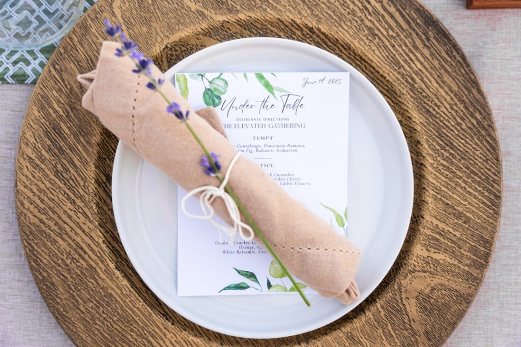 Ein gedeckter Tisch mit einer Serviette, die mit Lavendel und einer Einladungskarte dekoriert ist.