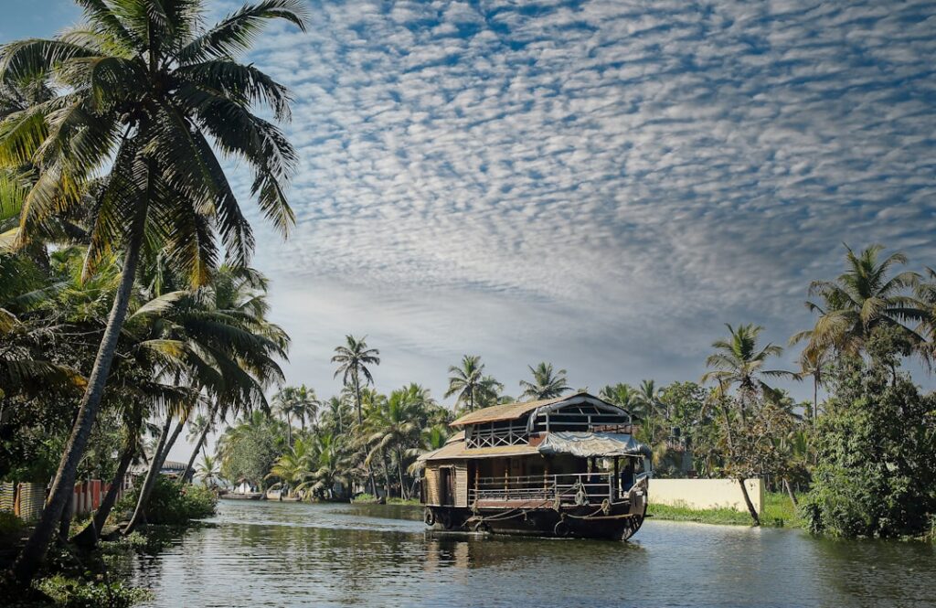 Traditionelles Hausboot auf einem ruhigen Wasserweg umgeben von Palmen und bewölktem Himmel.