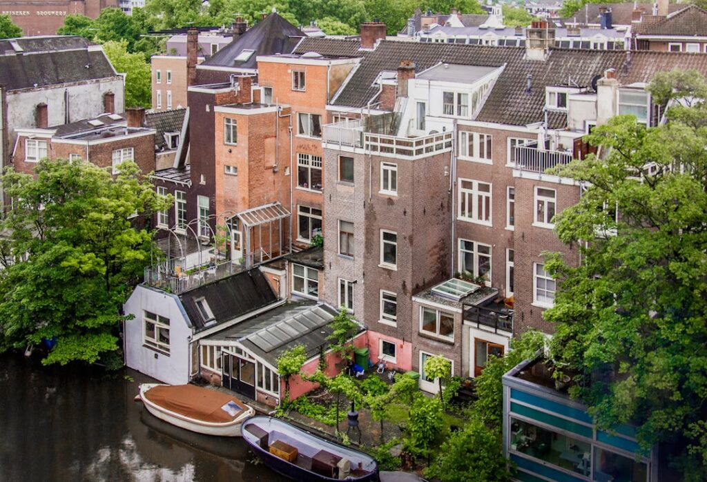 Blick auf eine Reihe von Wohngebäuden entlang eines Kanals in einer Stadt mit Bäumen und Booten.