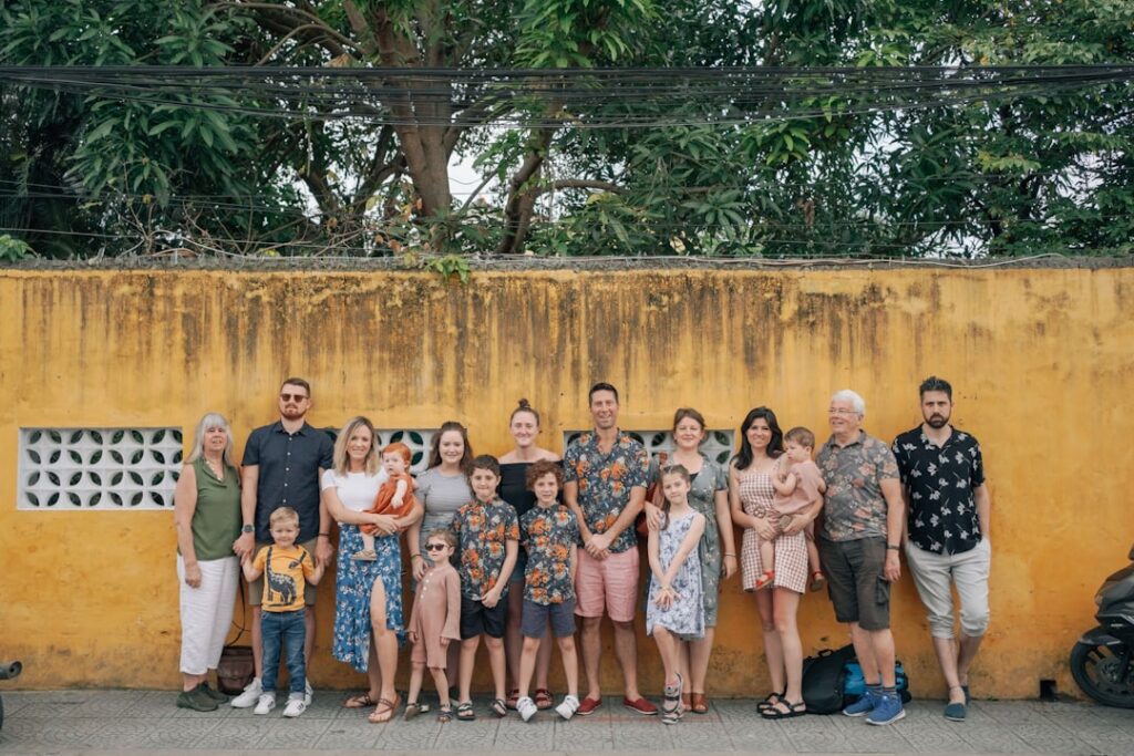 Gruppe von Menschen in bunten Hemden vor einer gelben Wand, bestehend aus Erwachsenen und Kindern.