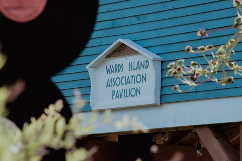 Schild der Wards Island Association Pavilion an einer blauen Wand mit Pflanzen im Vordergrund.