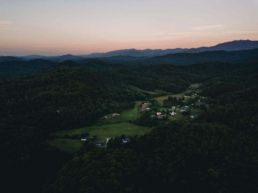 Luftaufnahme einer ländlichen Landschaft mit Hügeln und verstreuten Häusern in der Dämmerung.