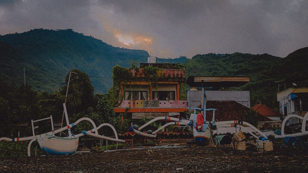 Verlassene Gebäude mit Booten und üppiger Vegetation in einer bergigen Umgebung.