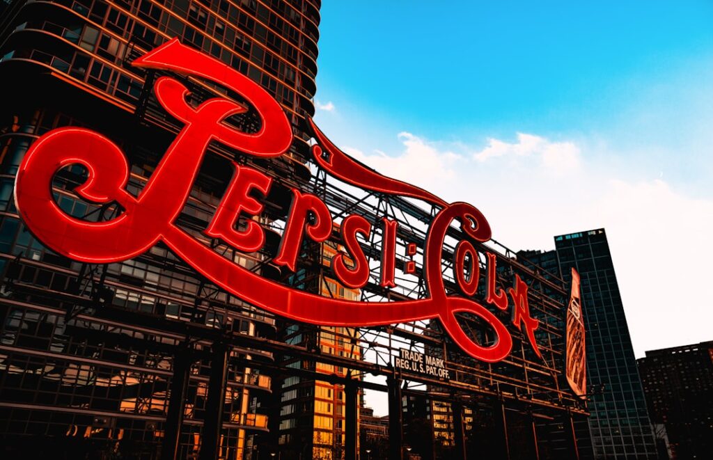 Rotes Pepsi-Cola-Schild an einem modernen Gebäude mit klaren Linien und blauem Himmel im Hintergrund.
