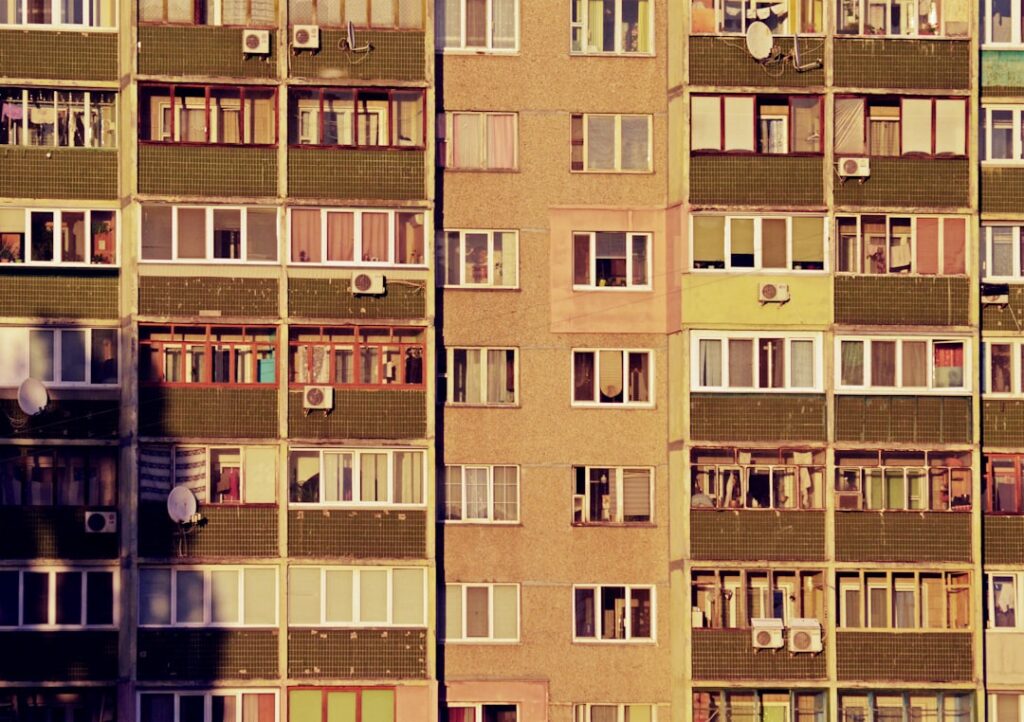 Fassade eines Wohngebäudes mit mehreren Fenstern und Klimaanlagen in verschiedenen Farben und Stilen.