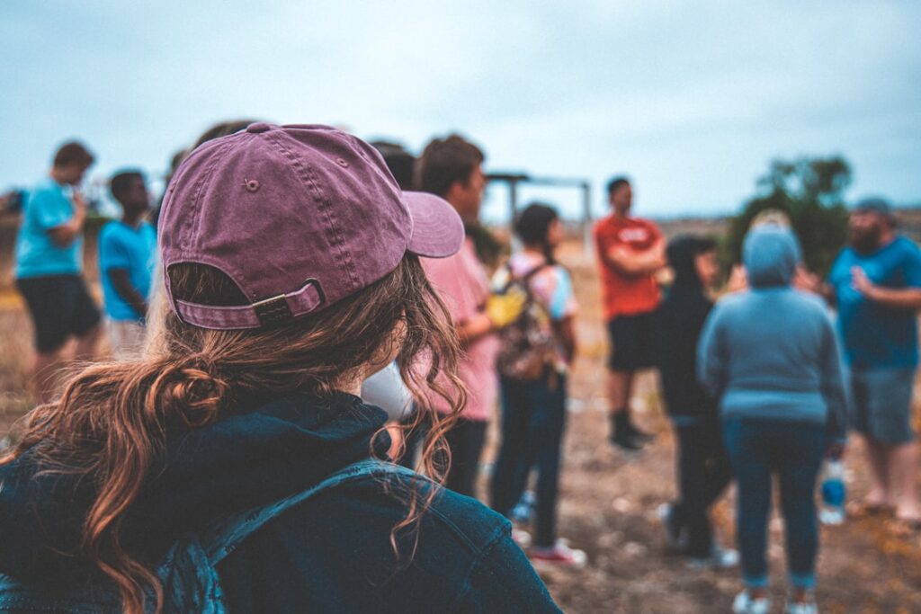 Person mit lila Kappe, die einer Gruppe von Menschen in einem offenen Bereich zuhört.