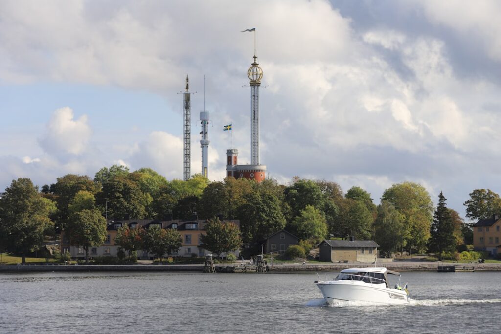 Boot auf einem Gewässer mit einer bewaldeten Küste und einem Aussichtsturm im Hintergrund.
