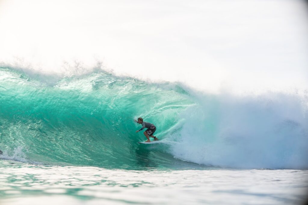 Surfer, der in einer großen grünen Welle auf einem Surfbrett reitet, mit spritzendem Wasser im Hintergrund.
