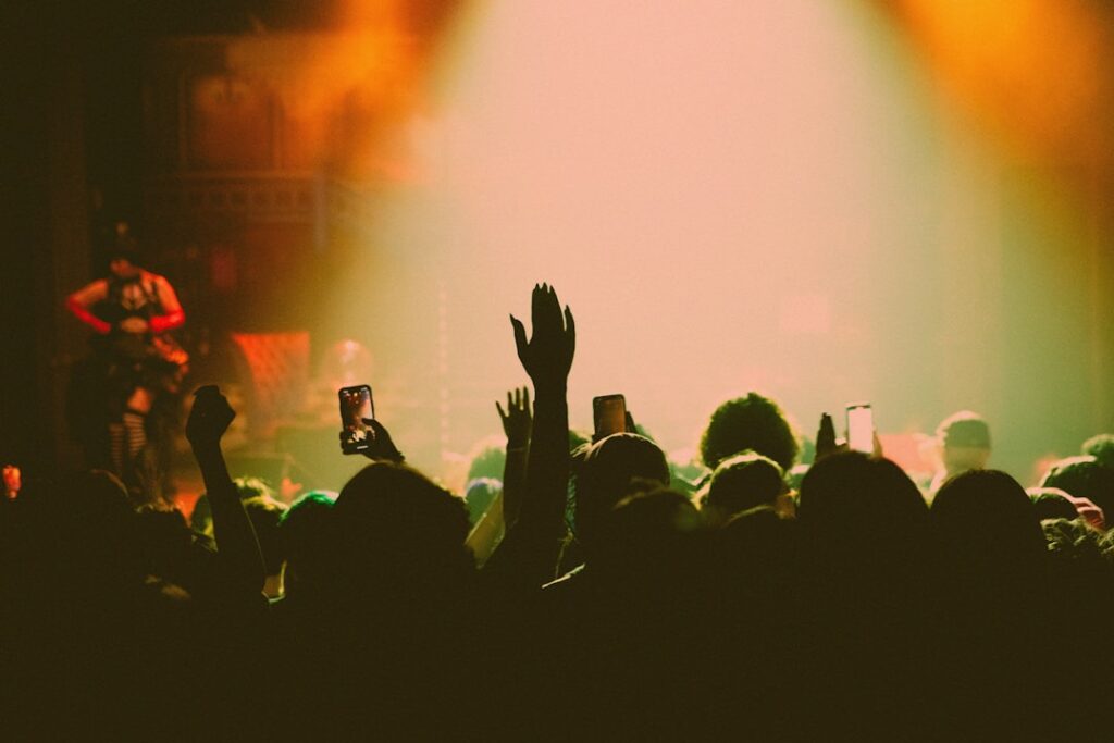 Menschenmenge mit erhobenen Händen und Smartphones in einem beleuchteten Veranstaltungsort.