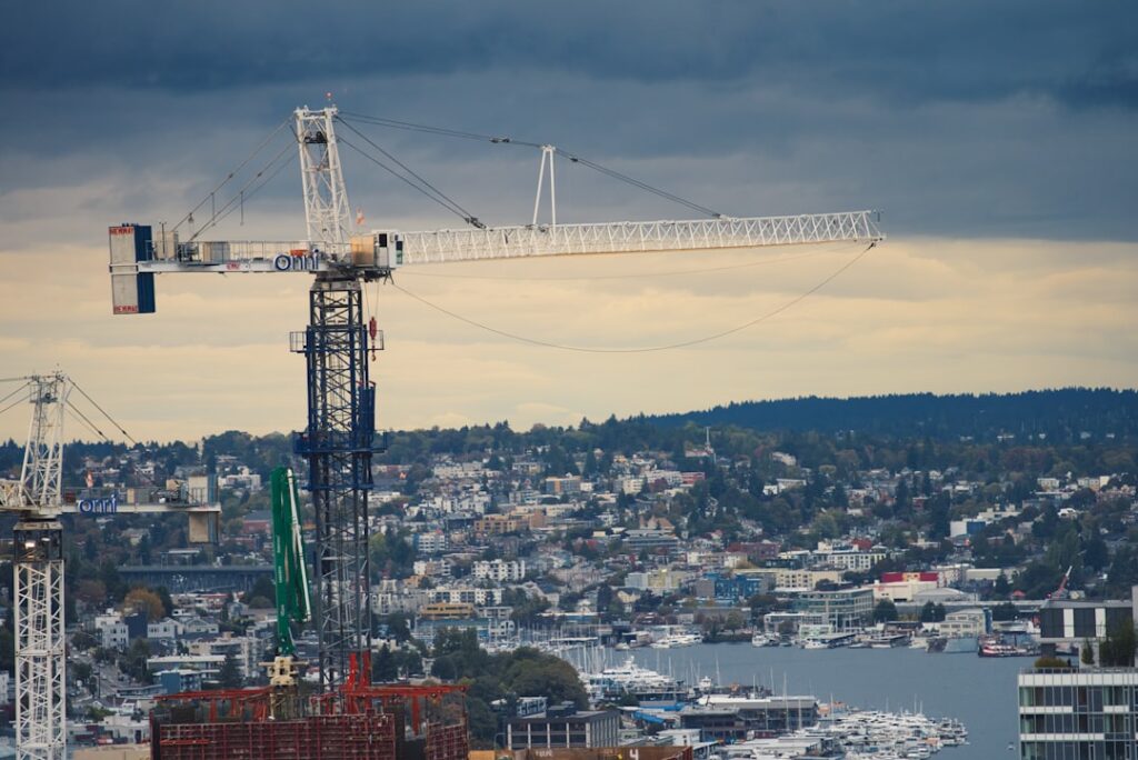 Baukran auf einer Baustelle mit Blick auf eine Stadtlandschaft und einen Hafen im Hintergrund.
