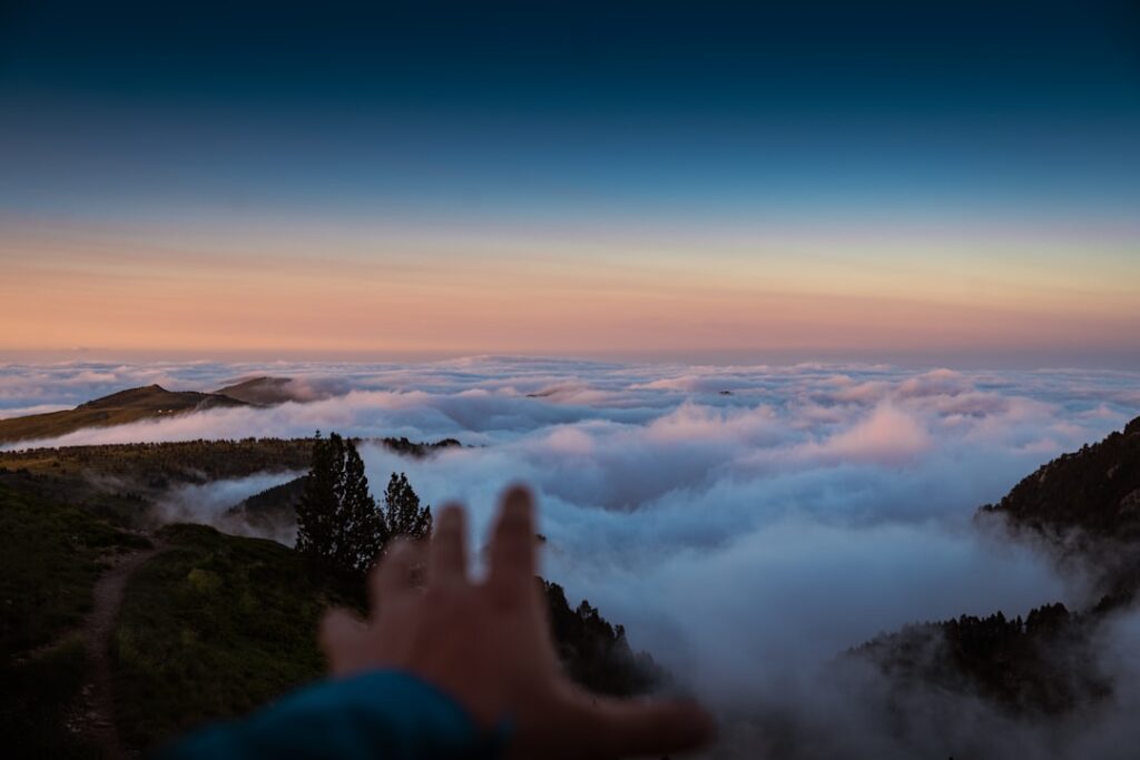 Hand, die auf eine Wolkendecke blickt, mit einem klaren Himmel im Hintergrund während der Dämmerung.