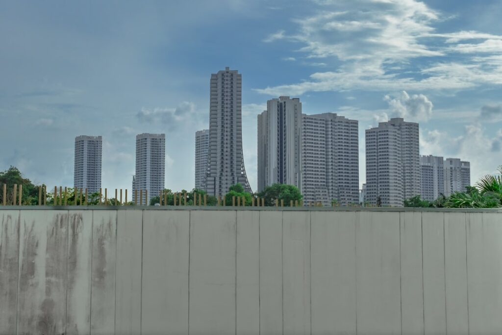 Hochhäuser in einer städtischen Umgebung unter einem bewölkten Himmel mit einigen grünen Elementen im Vordergrund.