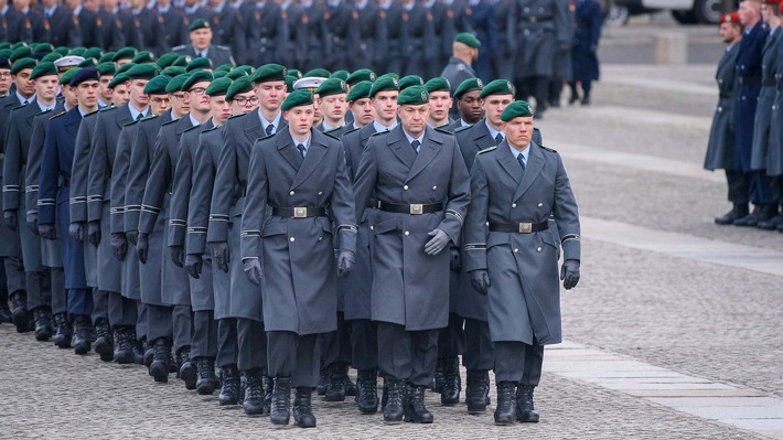 Soldaten der Bundeswehr in grauen Uniformen mit grünen Baretten während einer Parade auf einem Platz.