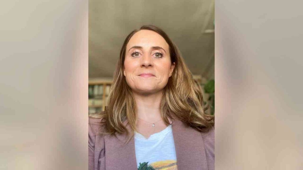 Frau mit langen, lockigen Haaren und einem lächelnden Gesicht, trägt ein helles Oberteil und einen Blazer.