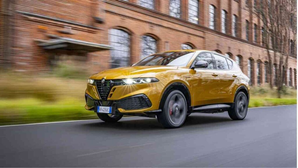 Alfa Romeo Tonale in gelber Farbe fährt auf einer Straße mit einer historischen Backsteinmauer im Hintergrund.