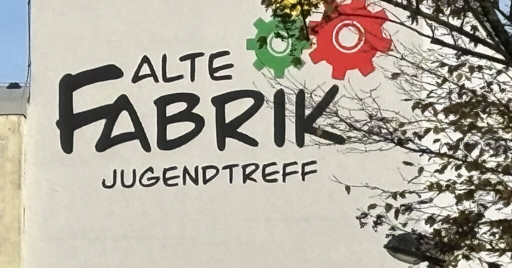 Wandmalerei mit dem Schriftzug 'Alte Fabrik' und zwei Zahnrädern in Rot und Grün.