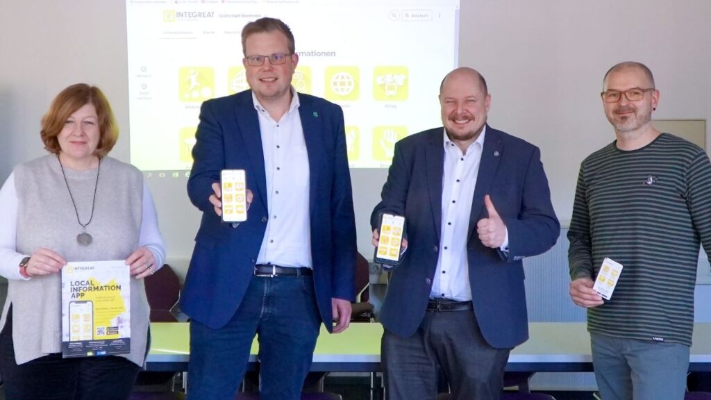 Vier Personen präsentieren eine lokale Informations-App mit Smartphones in einer Besprechung.