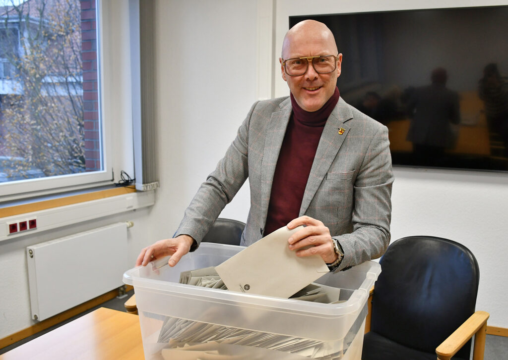 Mann mit Brille in grauem Anzug, der Umschläge aus einer durchsichtigen Box entnimmt.