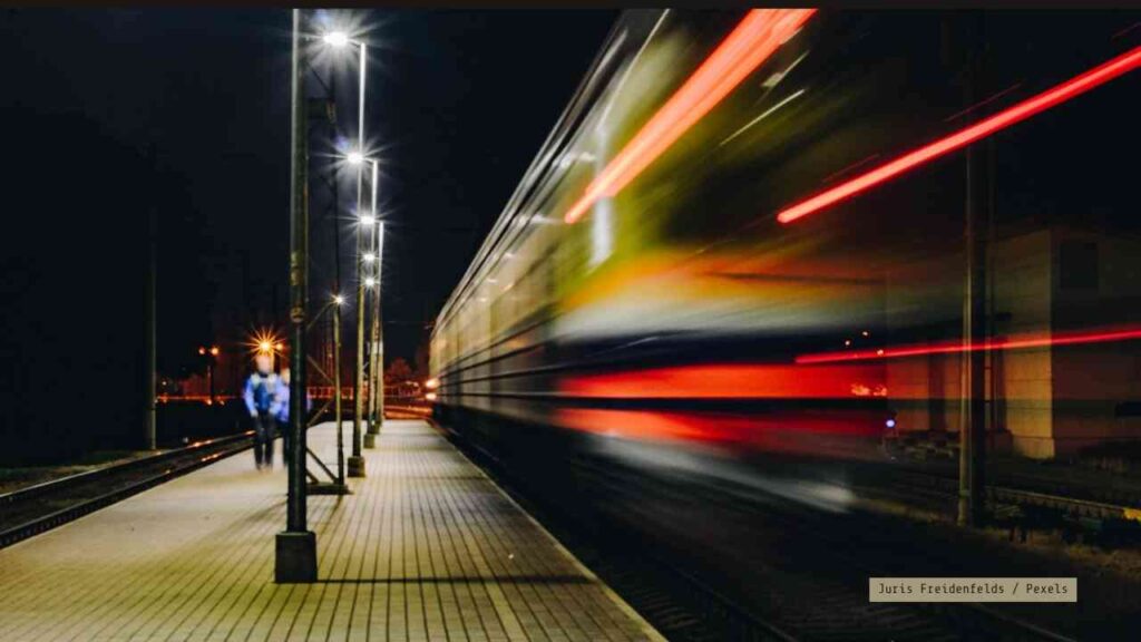 Ein Zug fährt schnell an einem Bahnhof vorbei, während eine Person auf dem Bahnsteig steht.