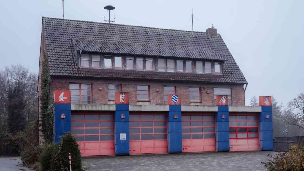 Ehemaliges Feuerwehrgebäude in Billerbeck mit rotem und blauem Garagentor und mehreren Fenstern.