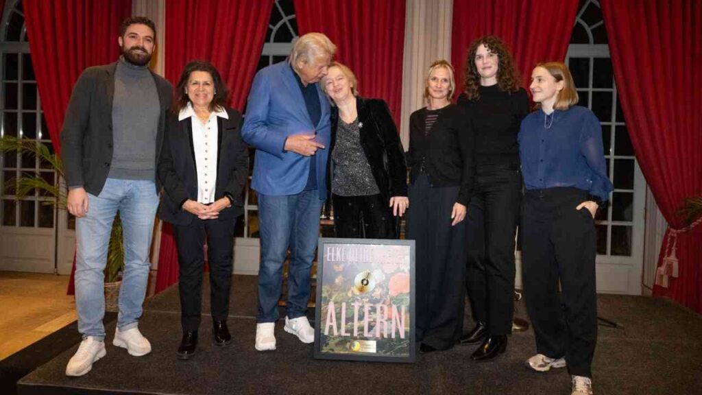 Gruppe von Personen auf einer Bühne bei einer Preisverleihung mit einem Plakat für das Buch 'Altern'.