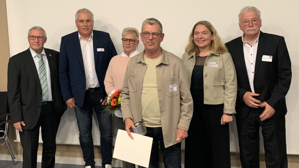 Gruppe von sechs Personen, die bei einer Veranstaltung zusammenstehen, einige mit Namensschildern.