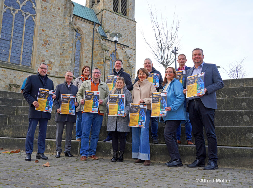 Gruppenfoto von Sponsoren und Organisatoren mit Plakaten für das Lichterfest vor einer Kirche.