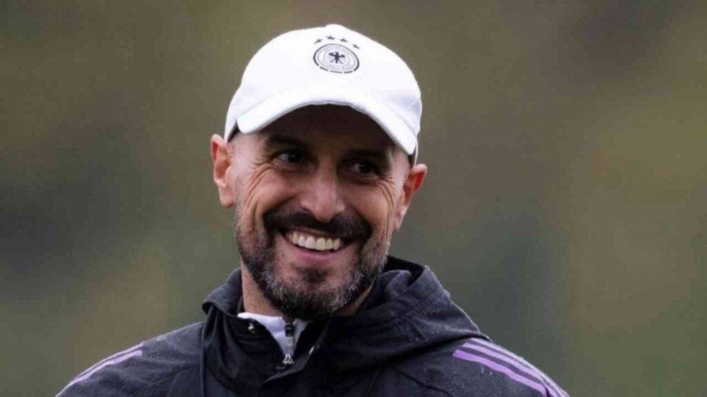Lächelnder Fußballtrainer mit einer weißen Kappe und einem schwarzen Trainingsanzug während des Trainings.