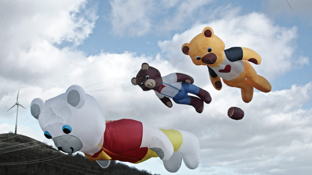 Drei große, aufblasbare Bären in verschiedenen Farben und Designs, die in den Himmel fliegen.