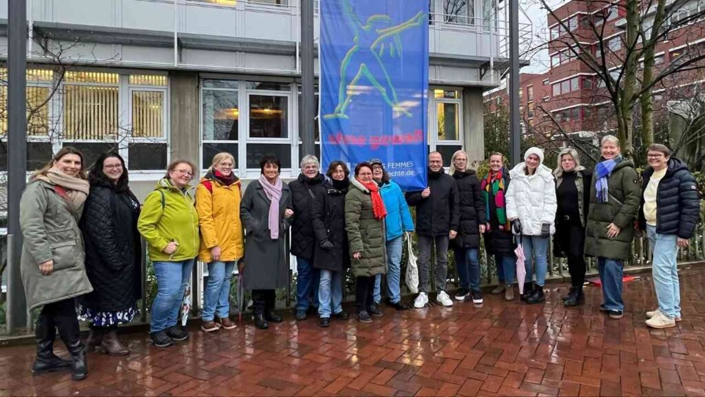 Gruppe von Menschen, die vor einem Gebäude mit einem großen Banner stehen, das eine stilisierte Figur zeigt.