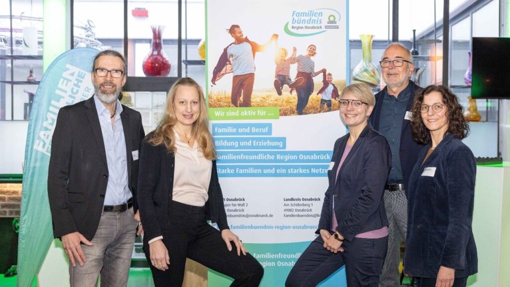 Gruppe von fünf Personen, die vor einem Banner des Familienbündnis Osnabrück stehen, mit verschiedenen Gesichtsausdrücken.