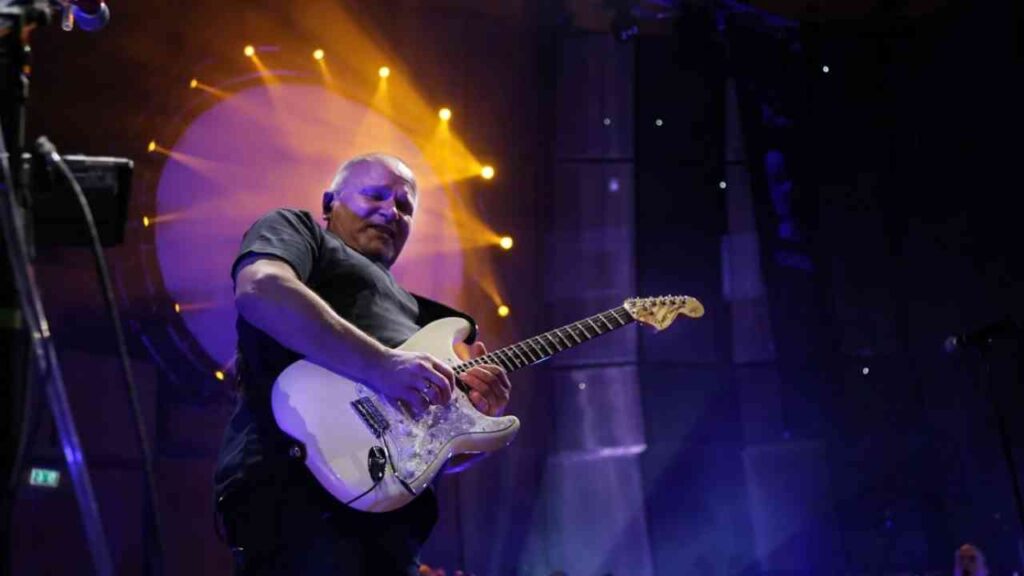 Mann spielt E-Gitarre auf einer Bühne mit bunten Lichtern im Hintergrund.