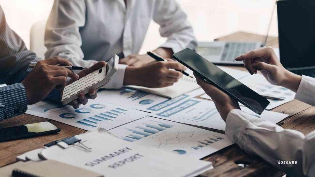 Mehrere Personen, die an einem Tisch mit Berichten, Diagrammen und elektronischen Geräten arbeiten.