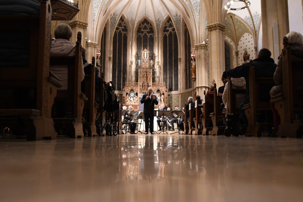 Ein Mann steht auf einer Bühne in einer Kirche und dirigiert ein Orchester während eines Konzerts.
