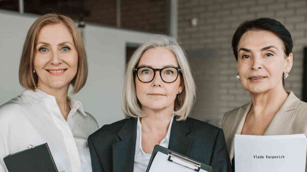 Drei Frauen in formeller Kleidung mit Aktenordnern und Notizblöcken in einem modernen Büro.