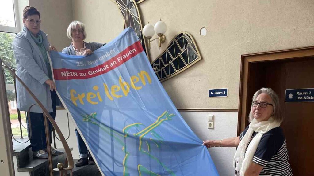 Drei Frauen halten ein Banner mit der Aufschrift 'frei leben' und dem Datum 25. November gegen Gewalt an Frauen.