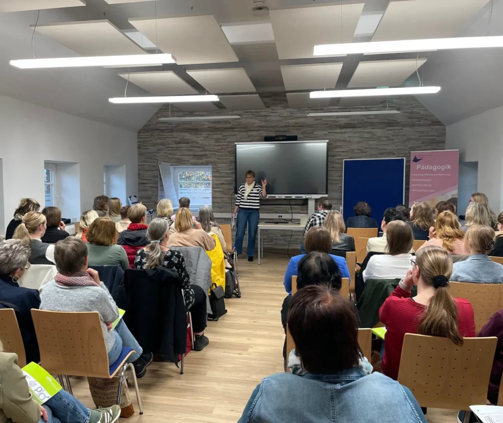 Eine Gruppe von Personen, die an einer Präsentation in einem Seminarraum teilnehmen, mit einer Referentin vorne.