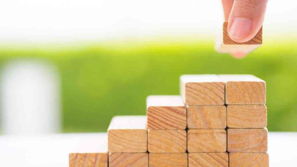 Hand, die einen Holzblock auf einen Stapel von Holzklötzen legt, die in einer Treppenform angeordnet sind.