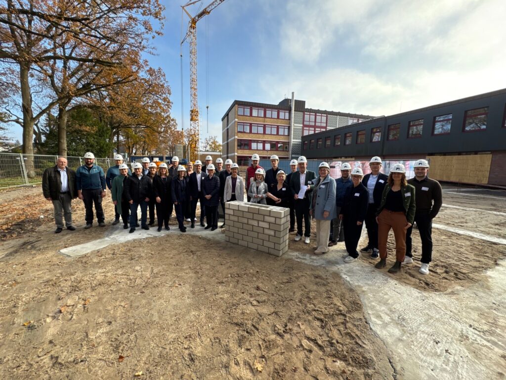 Gruppenfoto von Personen mit Bauhelmen, die um einen Grundstein auf einer Baustelle stehen.