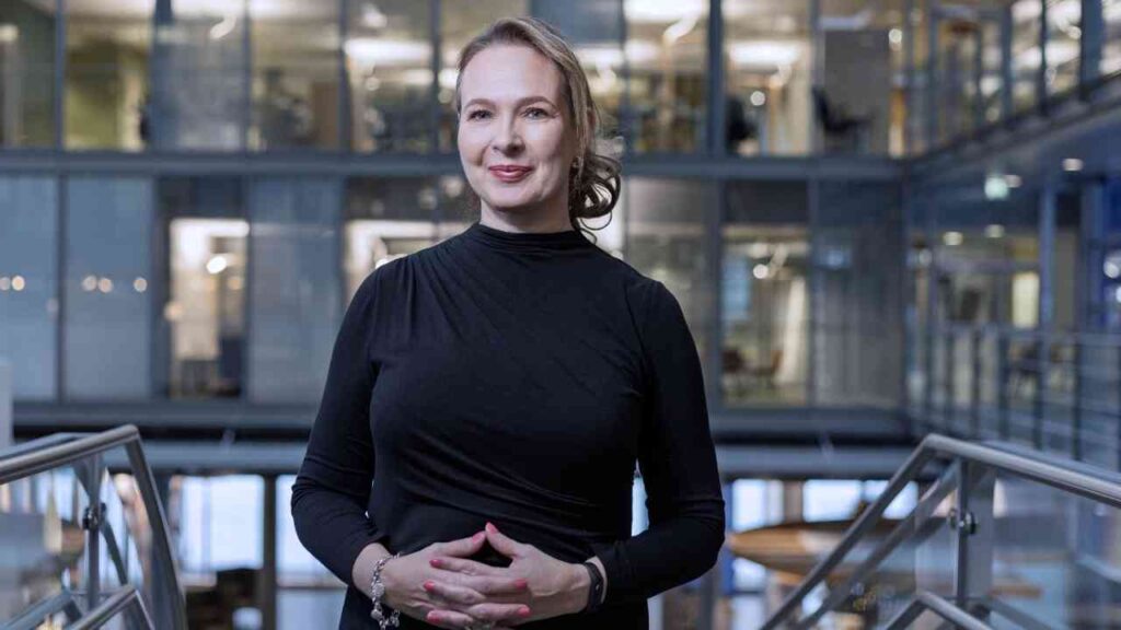 Frau in schwarzem Oberteil steht mit verschränkten Händen in einem modernen Bürogebäude.