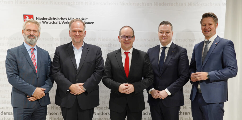 Fünf Männer in Anzügen stehen vor einem Hintergrund mit dem Logo des Niedersächsischen Ministeriums für Wirtschaft, Verkehr und Bauen.