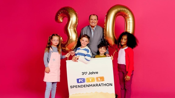 Vier Kinder und ein Erwachsener halten ein großes Banner zum 30. Jubiläum des RTL Spendenmarathons mit goldenen Zahlen.