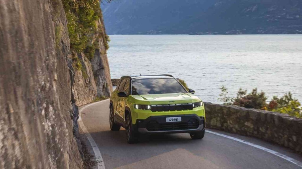 Jeep Compass in leuchtendem Grün fährt auf einer kurvenreichen Straße entlang eines Gewässers.